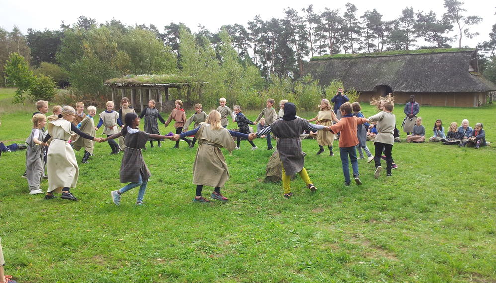 Børn danser i rundkreds på græsplæne