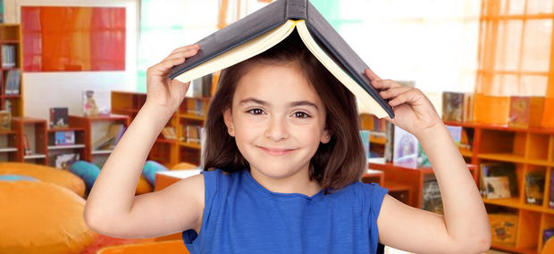 Mørkhåret smilende pige i blå bluse er på biblioteket og holder en udfoldet bog over hovedet, så det ligner et tag.
