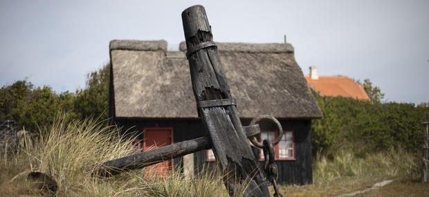 Kystmuseet Skagen, udendørs. Et stort anker i forgrunden og et lille sort hus i baggrunden.