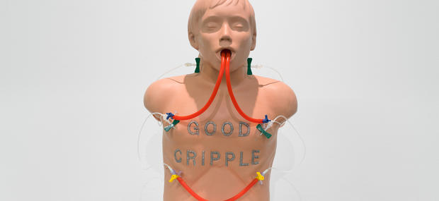 Værk af Panteha Abereshi fra 2023, der er fremstillet af en silicone førstehjælpsdukke med hospitalsslanger i halsen. På dens brystkasse står der værkets titel: GOOD CRIPLE.