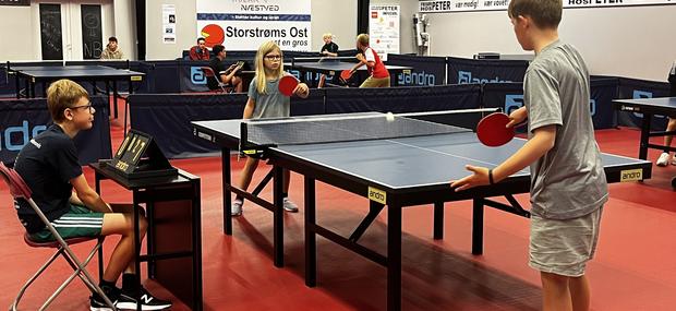 børn der er i gang med en bordtennisturnering ved flere borde.