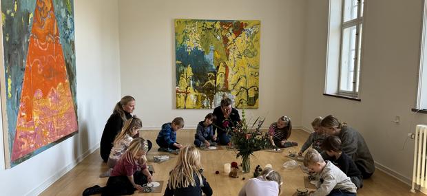 En gruppe børn og vokse sidder sammen og laver kreative ting, der passer til den udstilling de har set.