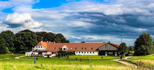 Smørum Golfklub på en solskinsdag med gul mark i forgrund og blå himmel med skyer i baggrunden