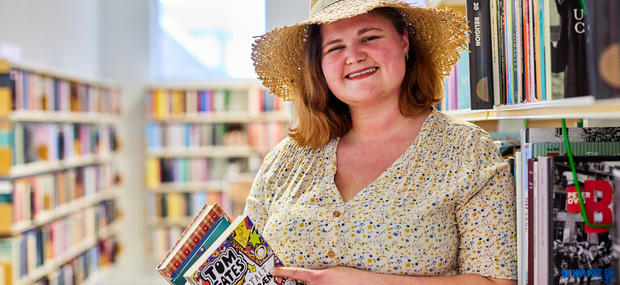 Bibliotekaren står med sommerhat og en stak bøger