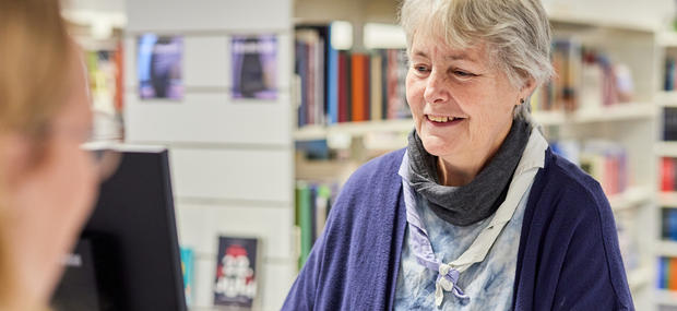 bibliotekaren står i skranken og tager imod en låner