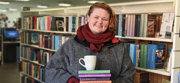 bibliotekaren står med en stakbøger, en kop kaffe og halstørklæde og jakke på