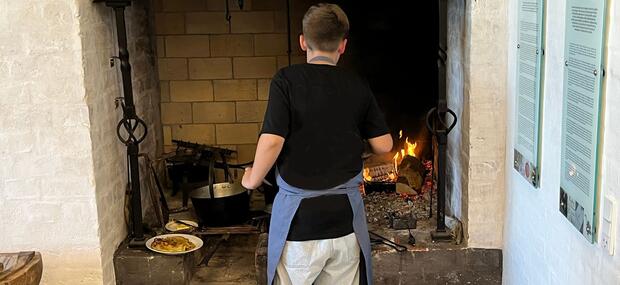 Billedet viser et barn der laver pandekager over åben ild på et ildsted