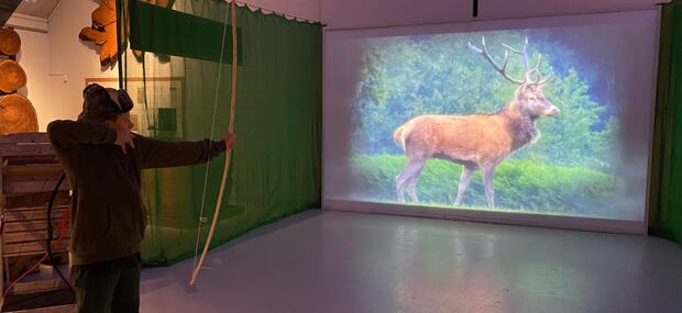Billedet viser et barn der skyder med bue og pil på en indendørs buebane på Det Grønne Museum