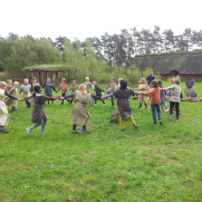 Børn danser i rundkreds på græsplæne