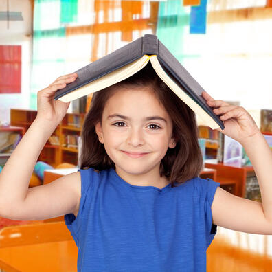 Mørkhåret smilende pige i blå bluse er på biblioteket og holder en udfoldet bog over hovedet, så det ligner et tag.