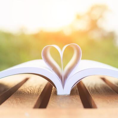 En bog ligger oplåset på et havebord udenfor i solnedgang. Midtersiderne er foldet som et hjerte.