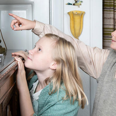 To børn - en dreng og en pige - i 1930'er stuen. De kigger begge op på et billede, mens drengen peger på det.