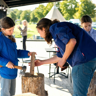 Elever er ved at lave en snelle med en økse. Underviseren instruerer. 