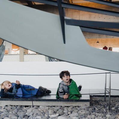 Eleverne kigger på det mindre fragtskib, Skuldelev 3, nedefra. Eleverne er i dyb samtale om skibet  iført kapper. 