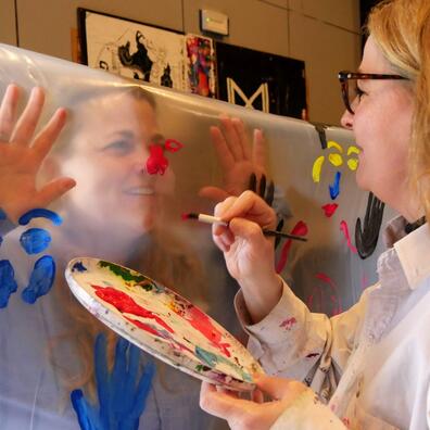 En pædagog maler en andens ansigt og hænder gennem klart, kraftigt plast