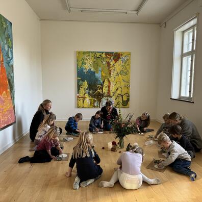 En gruppe børn og vokse sidder sammen og laver kreative ting, der passer til den udstilling de har set.