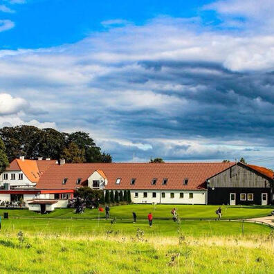 Smørum Golfklub på en solskinsdag med gul mark i forgrund og blå himmel med skyer i baggrunden
