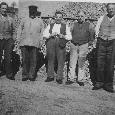 Fem mænd foran en stor bunke skærver, som de har slået med håndkraft.