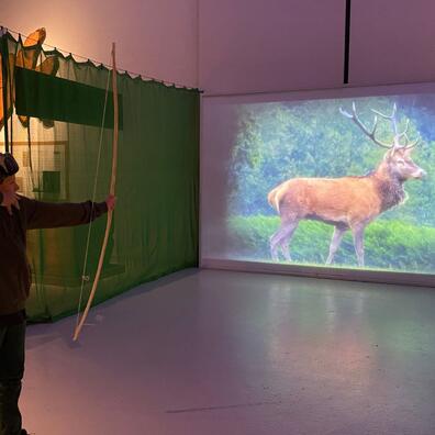 Billedet viser et barn der skyder med bue og pil på en indendørs buebane på Det Grønne Museum